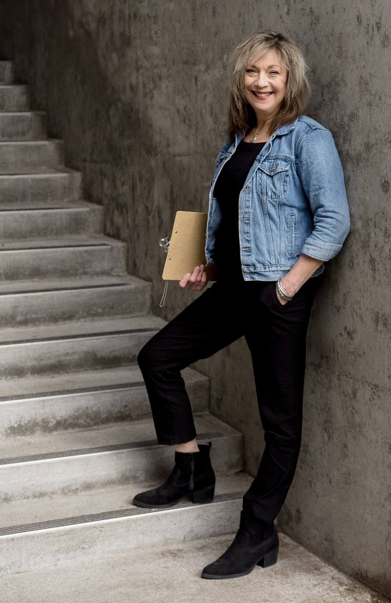 Stephanie Powers of YMCOT stand in front of staircase with a clipboard tucked under her arm.