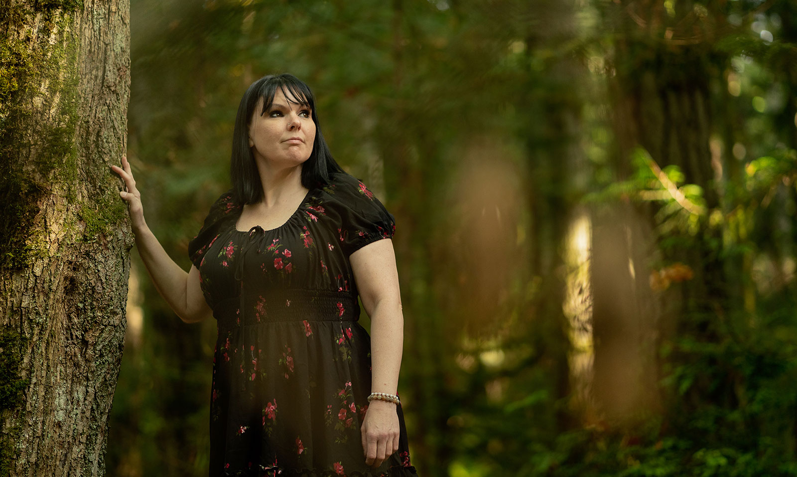 Woman in the woods leaning against a tree.